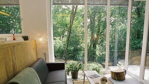 Un salón moderno con un sofá negro, una mesita blanca y un ventanal que ofrece vistas a zonas verdes.