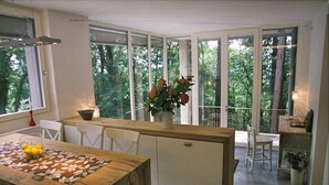 Una cocina moderna con una isla de madera, armarios blancos y ventanas amplias con vistas a la vegetación.