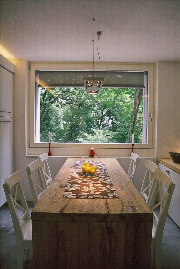 A dining table with chairs, a window with a view of trees, and a hanging light fixture.