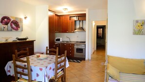 Cocina compacta con armarios de madera, microondas y horno. Se observa una mesa de comedor con sillas y mantel a cuadros.