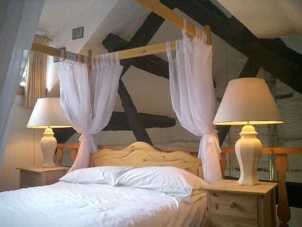Une chambre à coucher avec un lit à baldaquin, du linge de lit blanc, deux lampes de chevet et une tête de lit en bois.