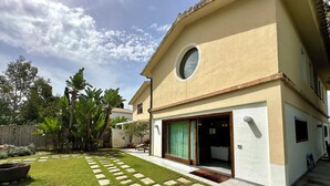 Une maison moderne à deux étages, dotée d’une pelouse bien entretenue, d’une fenêtre circulaire et d’une porte-fenêtre coulissante donnant sur un patio abrité.