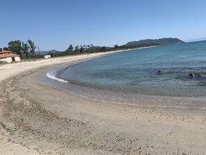 Une plage à l’eau claire, avec un rivage de galets et des montagnes qui se dessinent à l’horizon.