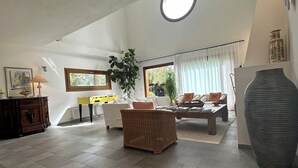 Un vaste espace de vie doté d’un plafond haut, d’une grande lucarne circulaire et d’une vue sur l’extérieur.