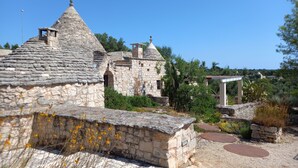 A stone building with a conical roof, surrounded by greenery and a gravel path. - 'Soul of Puglia' - A Rural Gem 3BR/3BA, A/C, WiFi, Hilltop w/ POOL & Views (Ostuni / Brindisi)