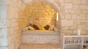 A stone-walled alcove with a cushioned bench and pillows, a shelf with metal cups, and a candle. - 'Soul of Puglia' - A Rural Gem 3BR/3BA, A/C, WiFi, Hilltop w/ POOL & Views (Ostuni / Brindisi)