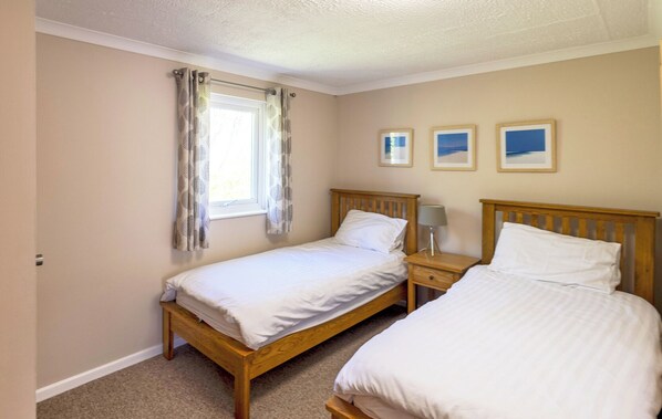A bedroom with two single beds, a window with curtains, and three framed pictures on the wall. - Quality Three Bedroomed House in Peaceful Seaside Village (Hayle)