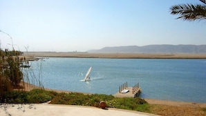 A calm lake with a sailboat, surrounded by a concrete patio and greenery.