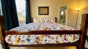 A bed with a floral bedspread, a mirror on the wall, and a view of the outdoors through a window.