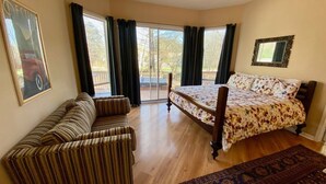 A bedroom with a bed, a sofa, a large window, and a door leading outside.