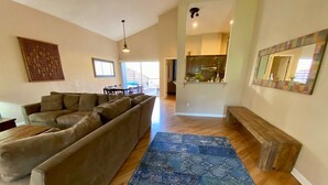 A spacious living room with a large sectional sofa, a blue patterned rug, and a wooden bench.
