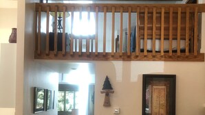 Ein geräumiger Wohnbereich mit hoher Decke, einer Holztreppe, einem braunen Ledersofa und einem gerahmten Kunstwerk an der Wand.