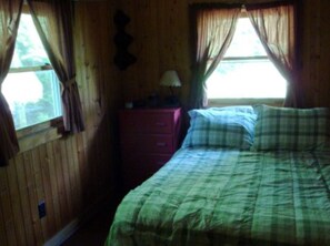 Une pièce en bois avec un lit, une commode et une fenêtre avec des rideaux.