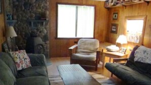 A cozy living room with a stone fireplace, a large window, and a comfortable seating area.