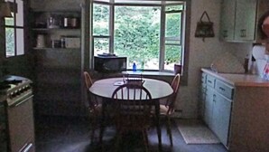 A compact kitchen with a dining table and chairs, a window with a view of greenery, and basic cabinetry.