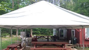 A covered outdoor area with picnic tables and a barbecue grill.