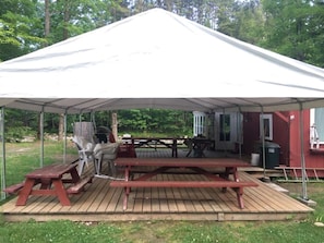 Un espace extérieur abrité, équipé de tables de pique-nique et d’un barbecue.