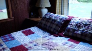 A bed with a quilt, a lamp, and a window with a view of the outdoors.