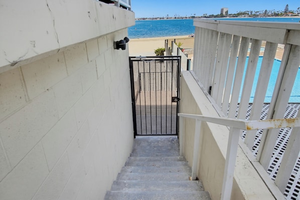 A concrete staircase leading to a gated entrance with a view of a beach and ocean.