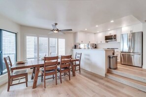 A modern kitchen with a central island, stainless steel appliances, and a dining area with wooden chairs.