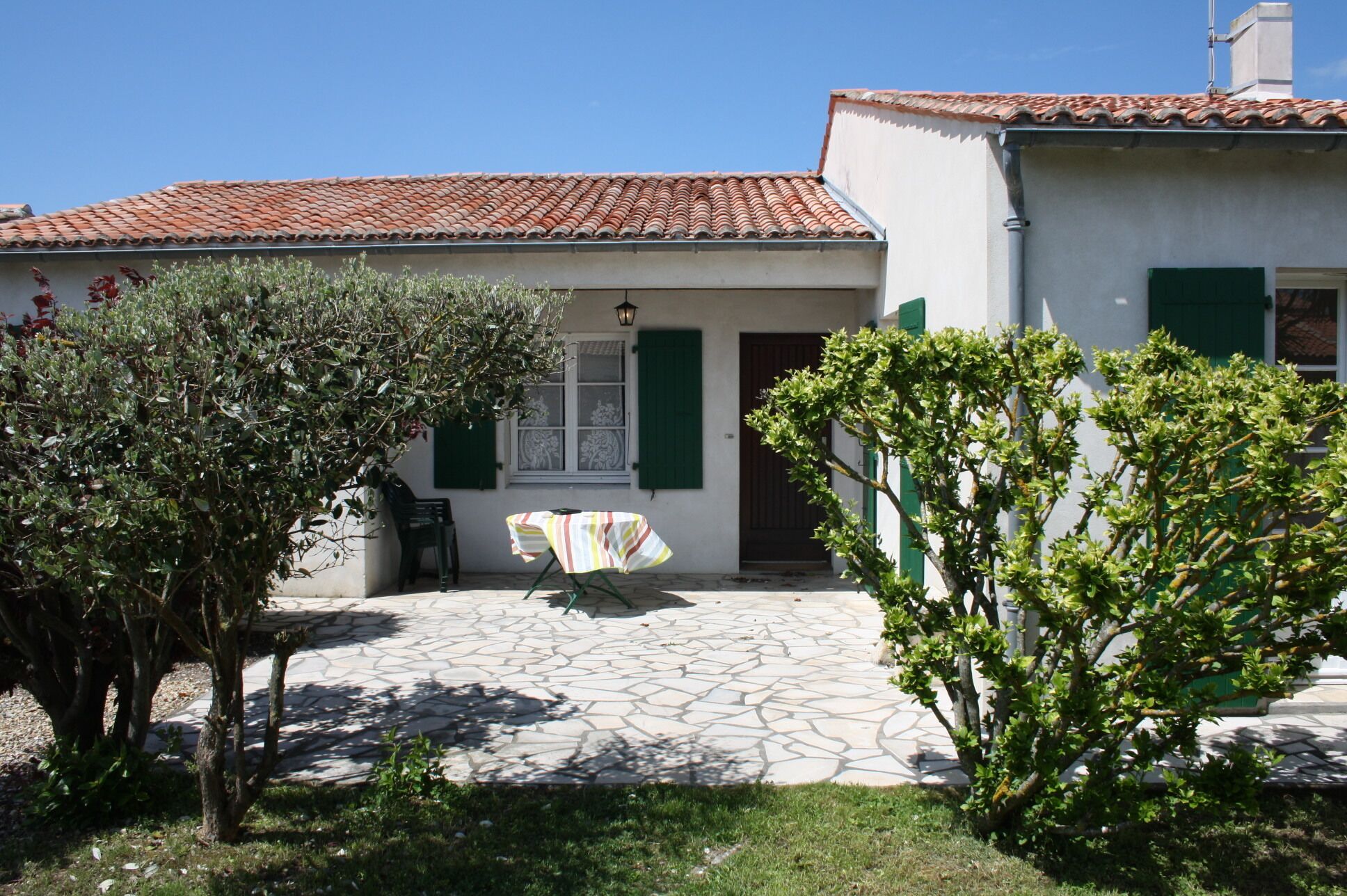 A house with a tiled roof, a stone patio, and a table with a striped tablecloth.