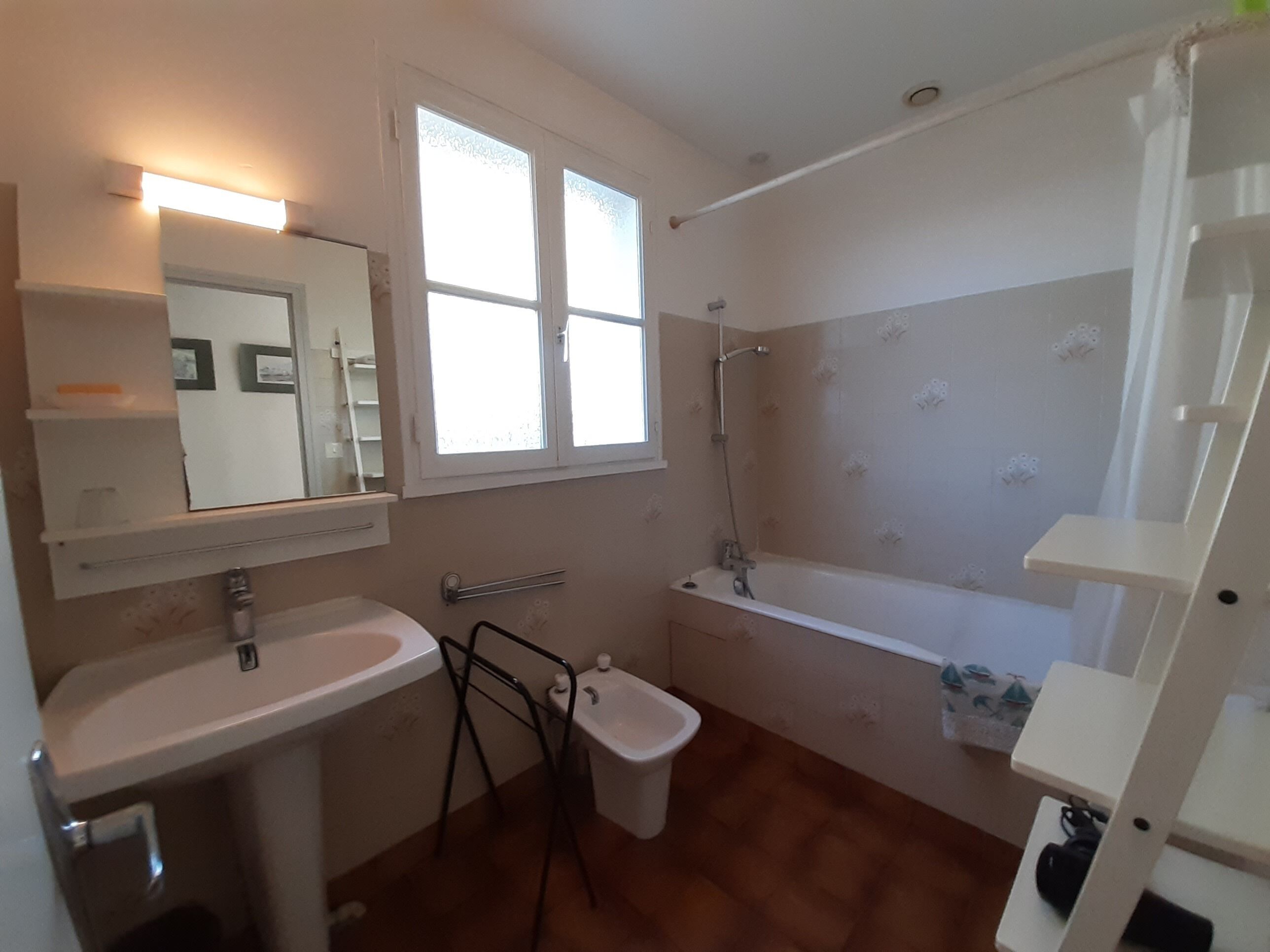 A bathroom with a sink, mirror, window, shower, and toilet.