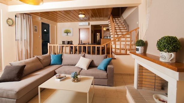 A cozy living room with a sofa, coffee table, and a fireplace. A wooden staircase leads to an upper level.