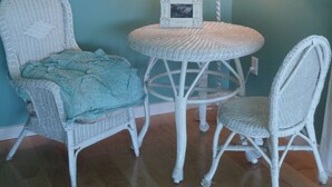 A room with a round table and two wicker chairs, a wall-mounted lamp, and a framed picture on the table. - A Relaxing Place To Have Fun In The Sun!  (Yakima)