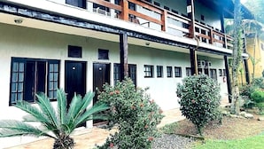A two-story building with balconies, a covered walkway, and a garden area with palm trees and shrubs. - 1 BEDROOM APARTMENT, COND. CLOSED, FACING THE POOLS AND 50M FROM THE BEACH (São Sebastião)