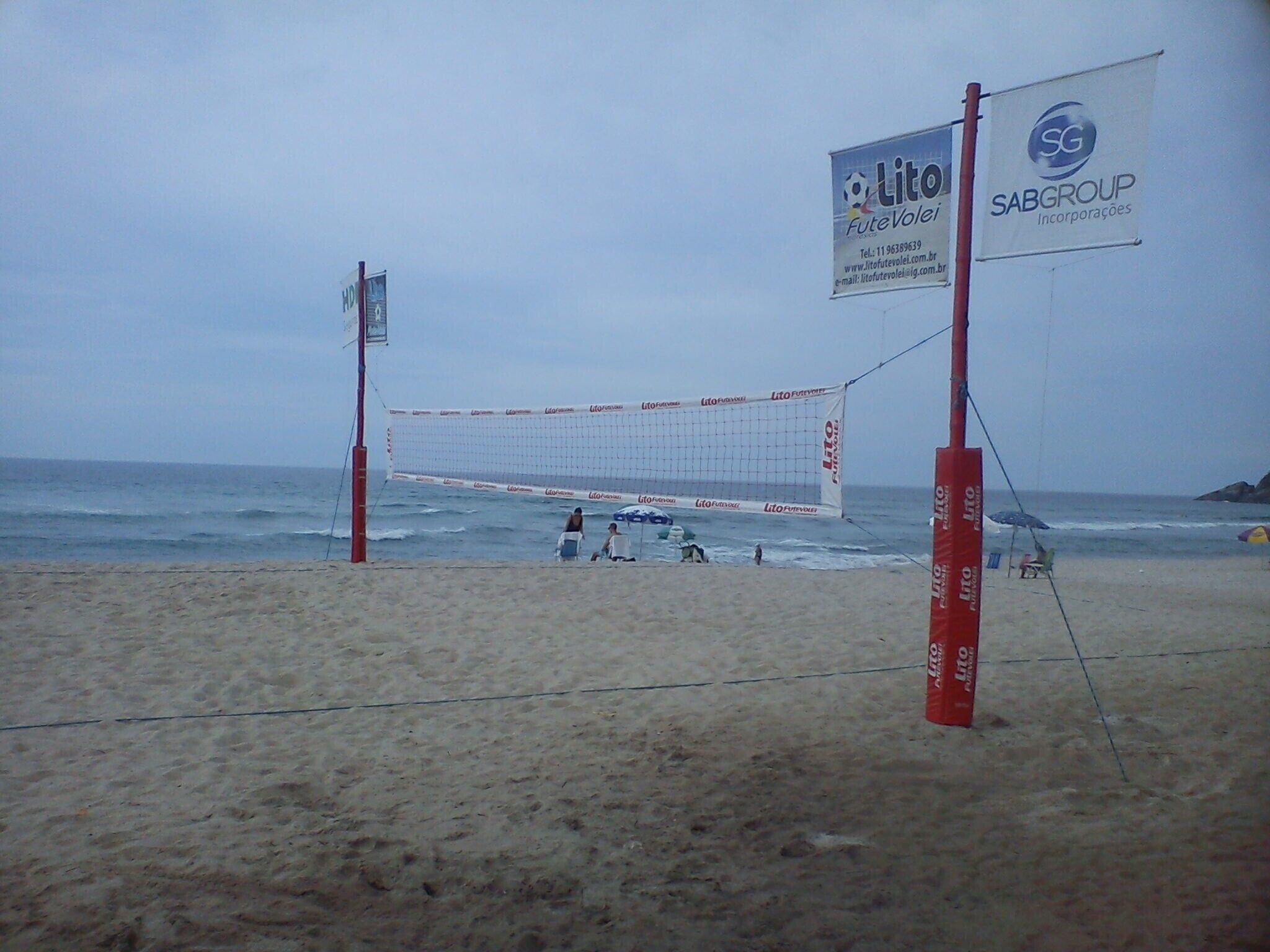 Una cancha de voleibol de playa con red, dos banderas y una playa arenosa.