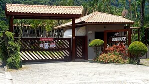 A gated entrance with a sign indicating '1 VAGA POR APARTAMENTO' and 'SUN HOUSE' with a number '2500'. - 1 BEDROOM APARTMENT, COND. CLOSED, FACING THE POOLS AND 50M FROM THE BEACH (São Sebastião)