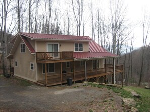 Een chalet van twee verdiepingen met een rood dak, een balkon op de bovenverdieping en een overdekte veranda.
