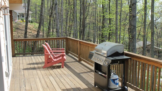 Une terrasse en bois avec un barbecue et deux chaises Adirondack rouges.