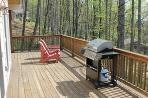 A wooden deck with a grill and two red Adirondack chairs. - Contemporary Mountain Vacation Home (Waynesville)