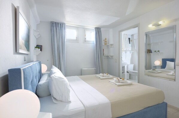 A hotel room with a bed, a large mirror, a window with curtains, and a bathroom visible through an open door.