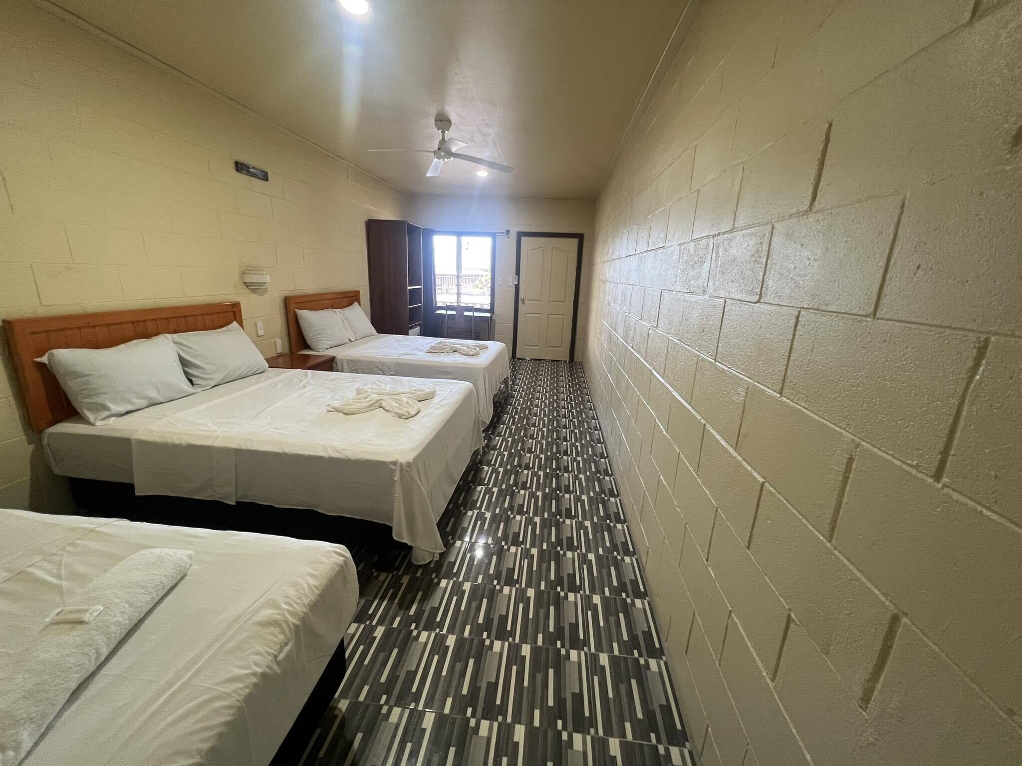 A hotel room with three beds, a ceiling fan, a patterned floor, and a door leading to another room.