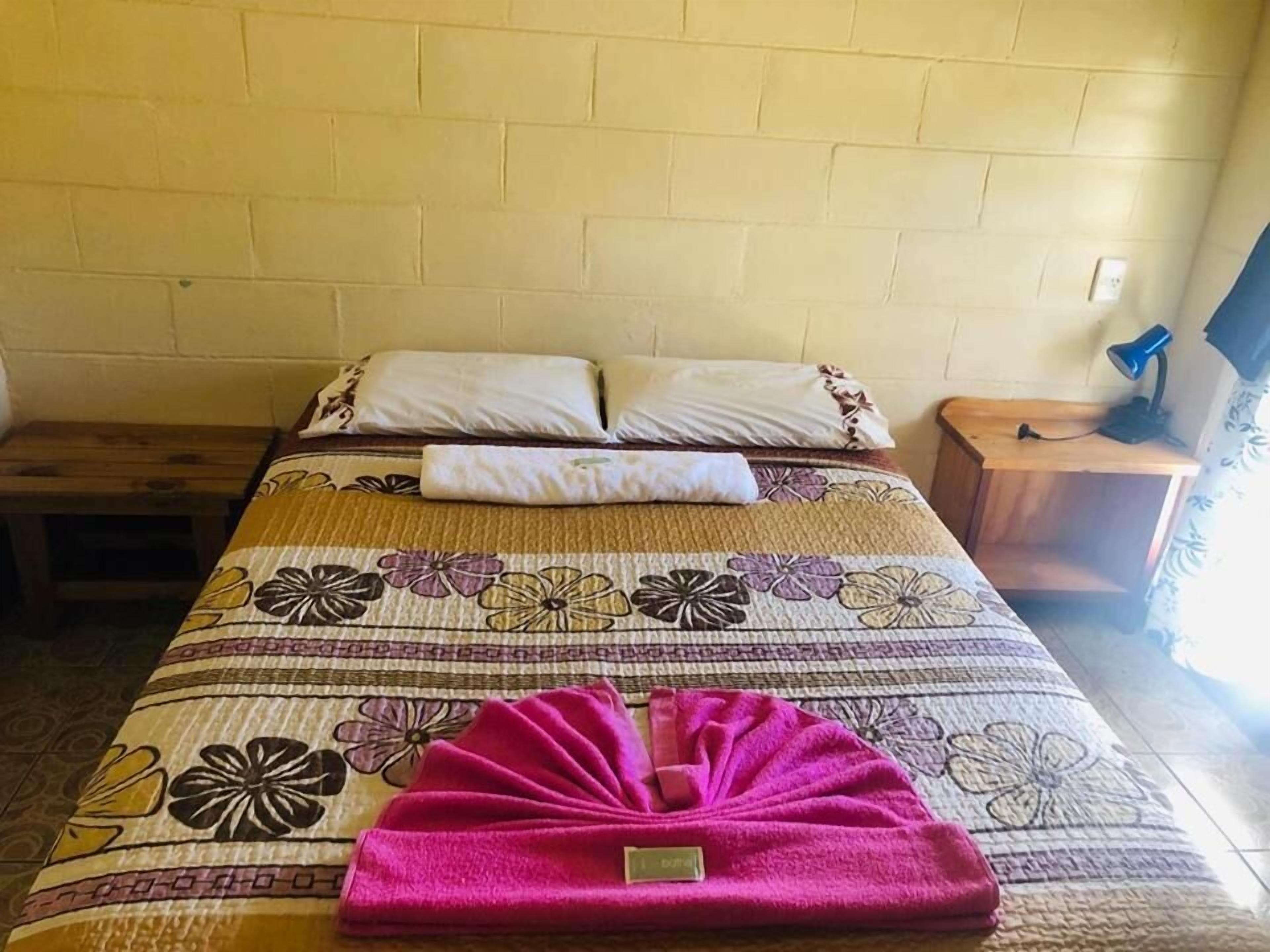 Ein Bett mit Blumenmuster, zwei Kissen, ein gefaltetes Handtuch und ein Nachttisch mit Lampe.