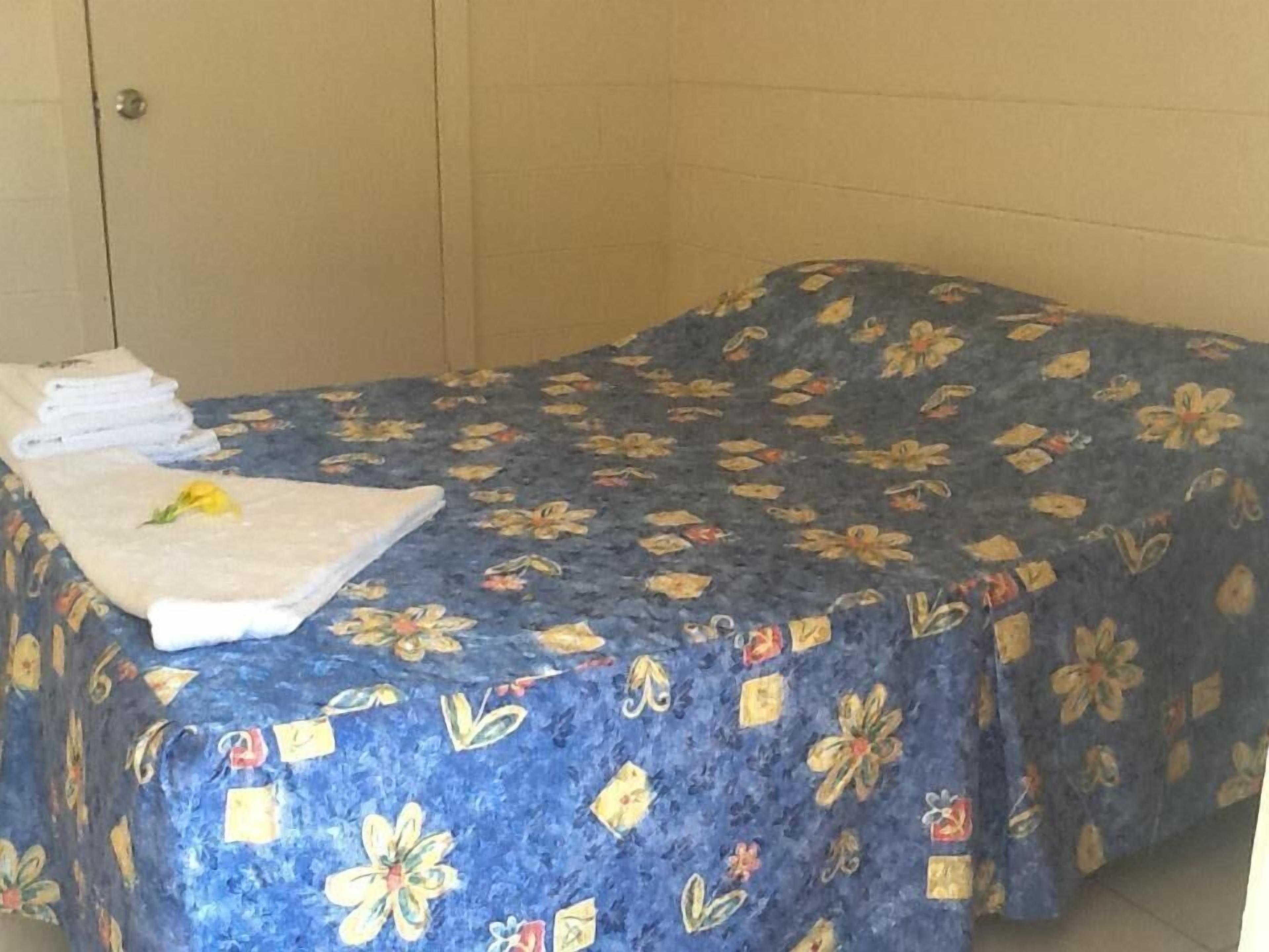 A room with a bed covered in a floral-patterned bedspread, a neatly folded white towel, and a yellow flower on the bed.