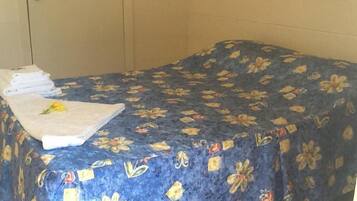 A room with a bed covered in a floral-patterned bedspread, a neatly folded white towel, and a yellow flower on the bed.