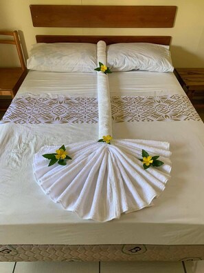 A neatly made bed with a towel arranged in a fan shape and a decorative flower. - Transit Motel - Hostel (Mulifanua)