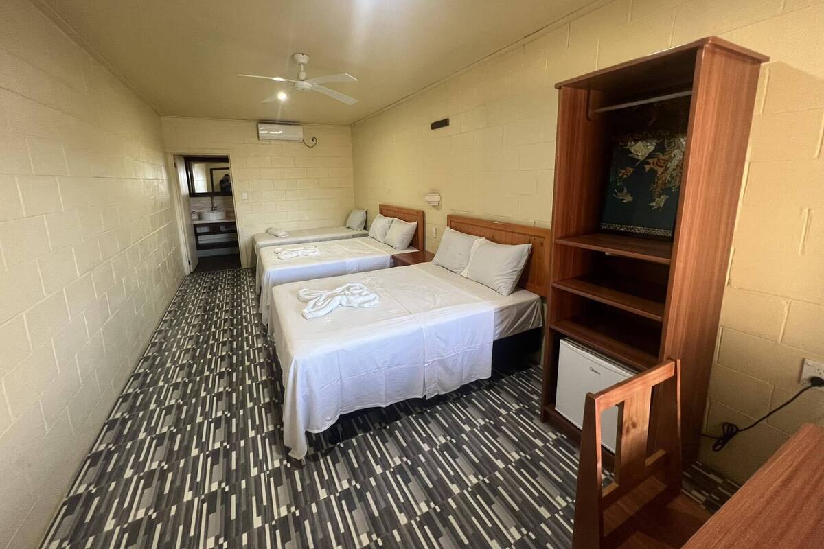 A hotel room with three beds, a ceiling fan, a small TV, and a patterned floor.