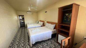 A hotel room with three beds, a ceiling fan, a small TV, and a patterned floor.