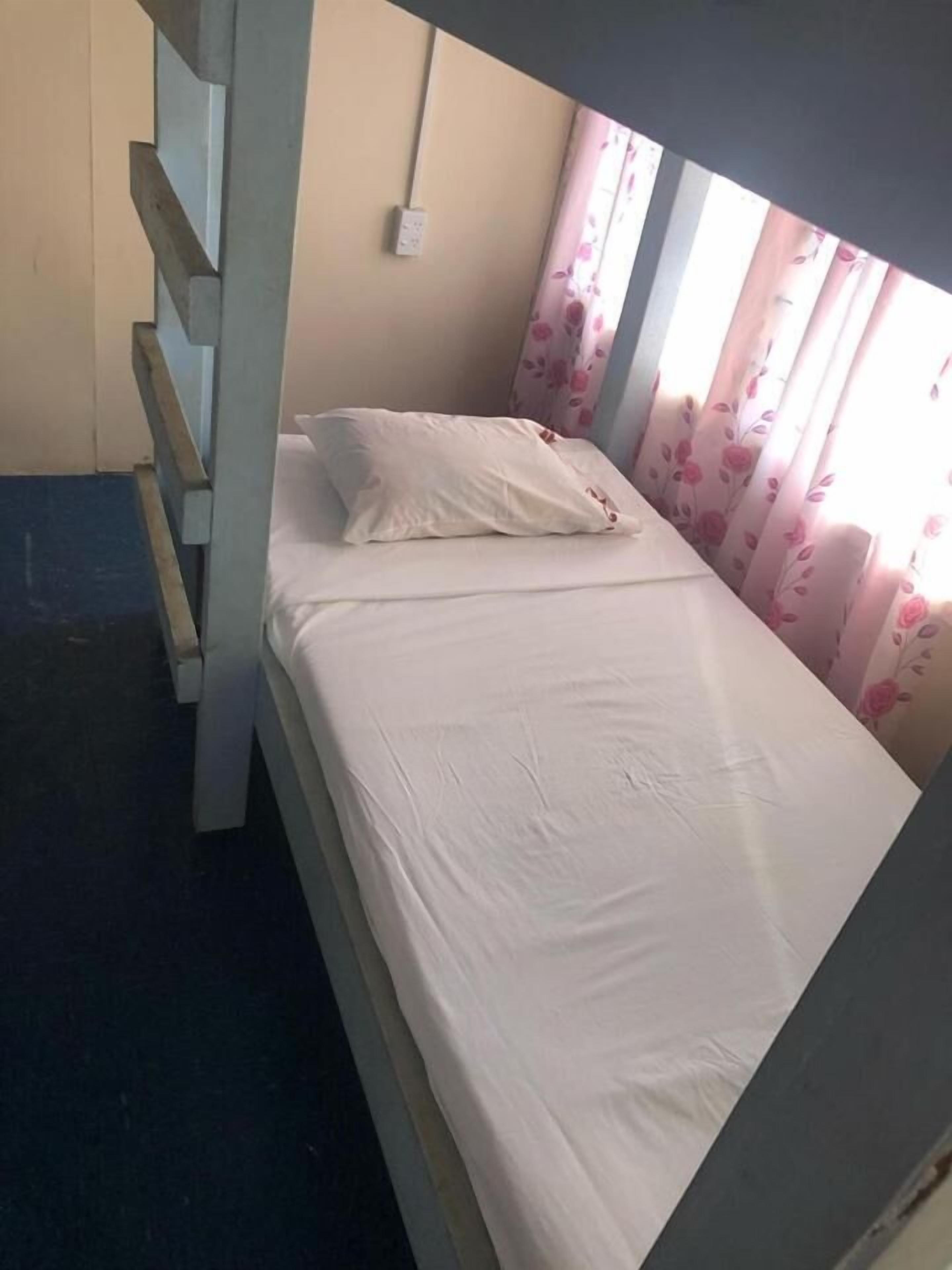 Uma cama beliche com colchão e travesseiro brancos, uma tomada na parede e cortinas florais.