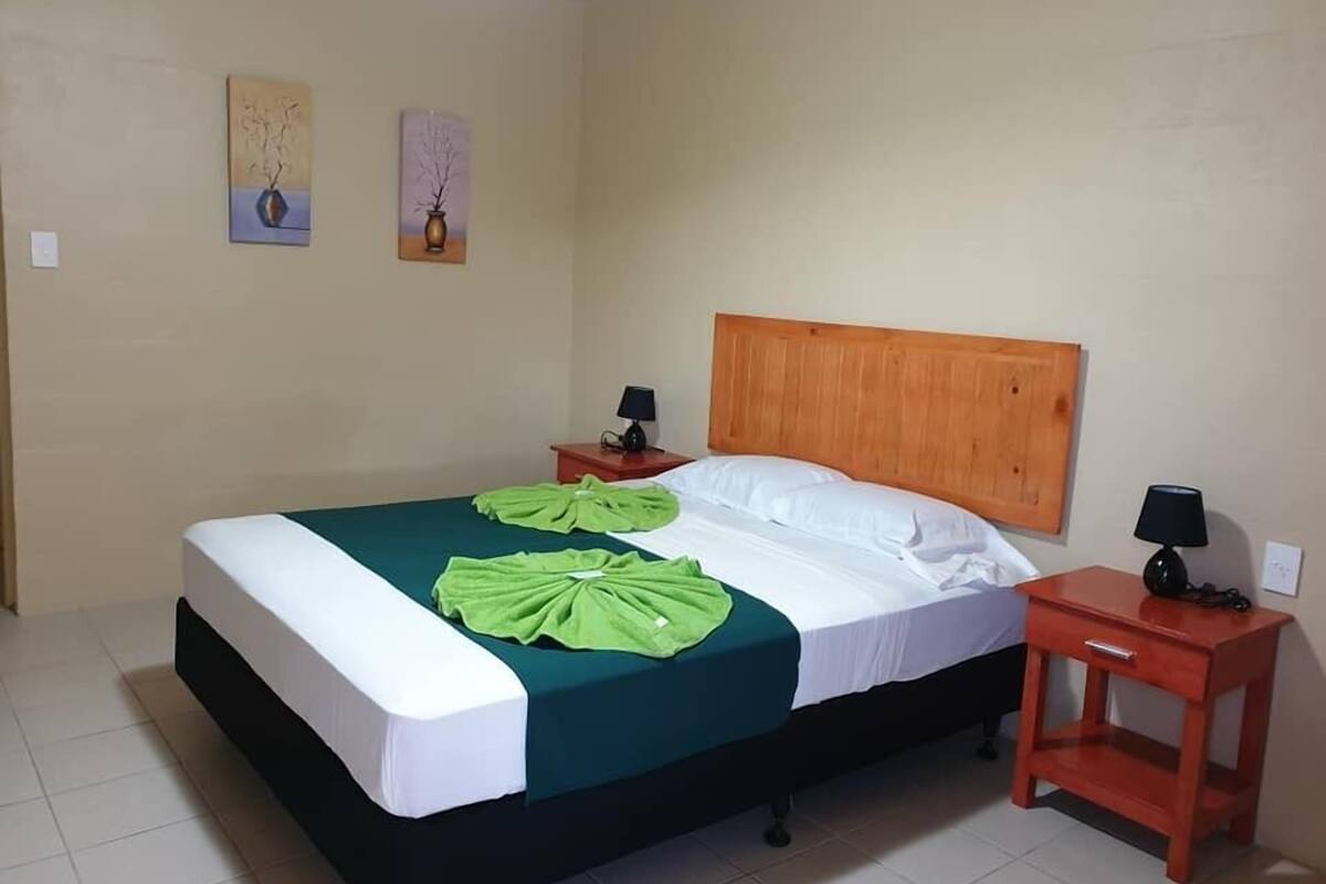A neatly made bed with green and white linens, a wooden headboard, and two bedside tables with lamps.