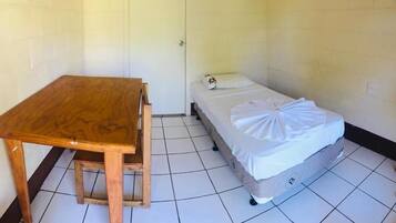 A small, single-room accommodation with a wooden table and a bed with a white blanket.