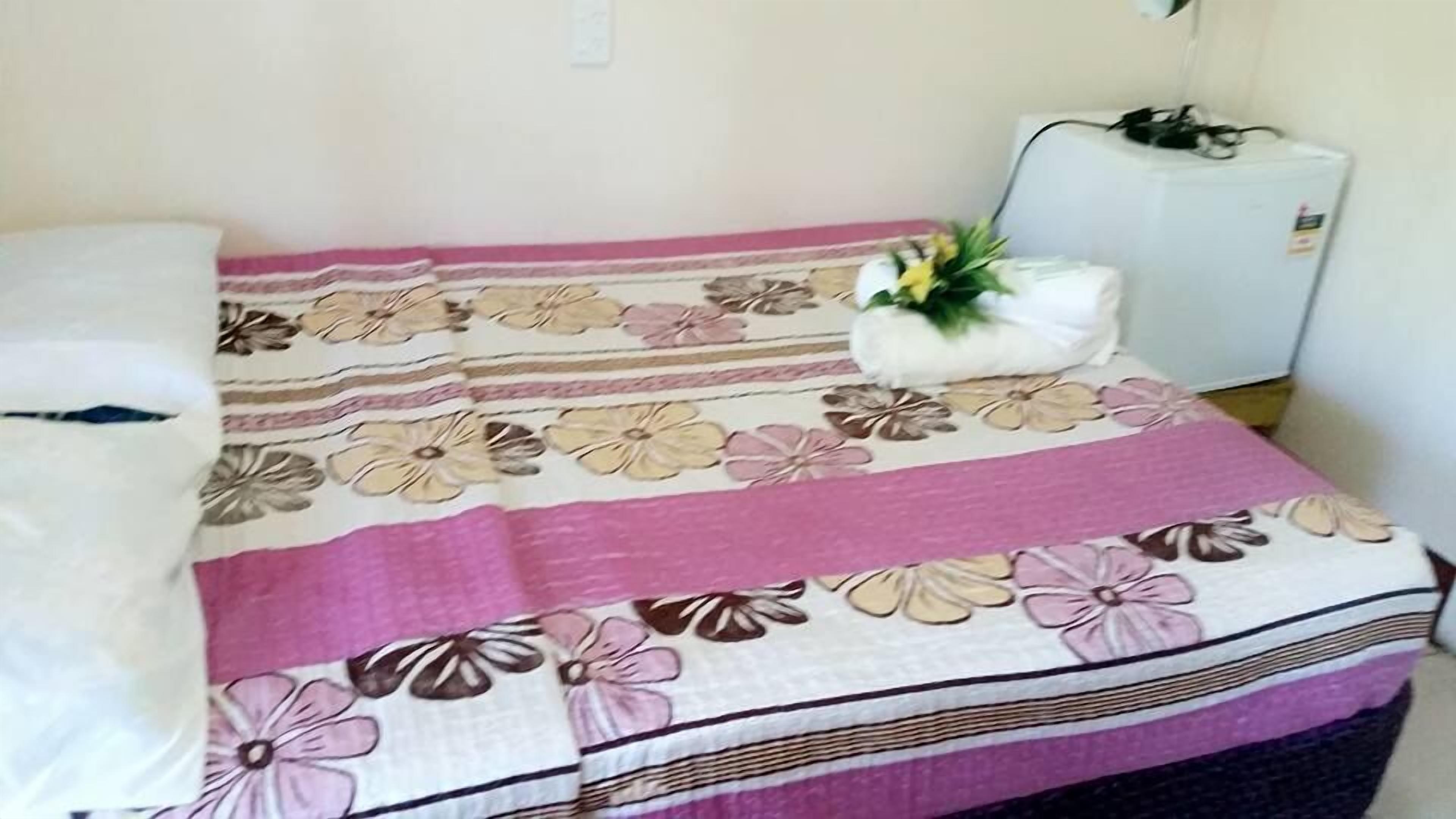 A bed with a floral-patterned bedspread, a white pillow, and a small plant on the side.