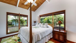 A bedroom with a four-poster bed, large windows, wooden flooring, and a ceiling fan.