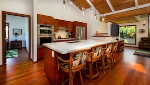 A modern kitchen with a large island, wooden flooring, and a high ceiling with skylights.