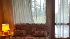 Ein Schlafzimmer mit einem Bett, einer Lampe und großen Fenstern mit durchsichtigen Vorhängen.