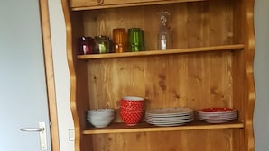 Ein Holzschrank mit Regalen, der verschiedene Küchenutensilien beherbergt, darunter Teller, Tassen und Gläser.